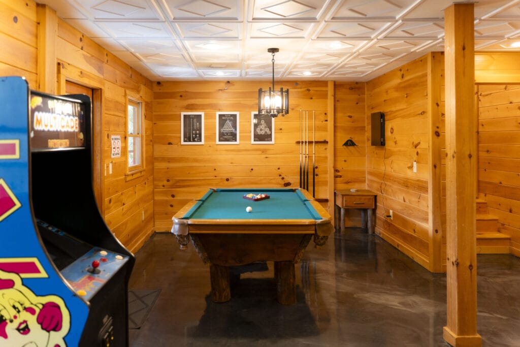 Entire game room of the Lincoln Logs Cabin, with pool sticks, a pool table, and an arcade machine
